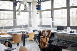 Engineer using tablet PC sitting on chair at workshop - JOSEF23622