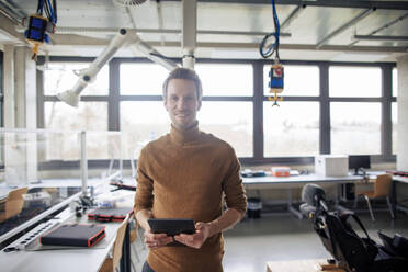 Lächelnder Ingenieur, der ein Tablet hält und in einer Werkstatt steht - JOSEF23630