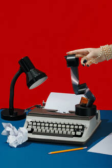 Hand eines Schriftstellers, der ein Filmnegativ neben einer Schreibmaschine auf dem Schreibtisch hält - RDTF00010