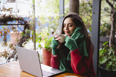 Lächelnde Frau genießt Kaffee in einem Café neben einem Laptop - AMWF02040