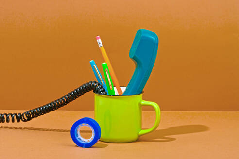Telephone receiver and office supplies in mug against orange background - RDTF00023