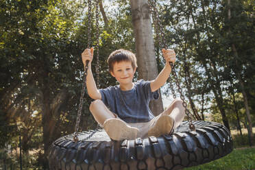 Smiling boy swinging on tire at park - ELMF00003