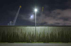 Niederlande, Südholland, Rotterdam, Alte Hafenkräne von hinter der Mauer bei Nacht gesehen - MKJF00034