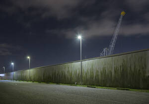 Niederlande, Südholland, Rotterdam, Alte Hafenkräne von hinter der Mauer bei Nacht gesehen - MKJF00035