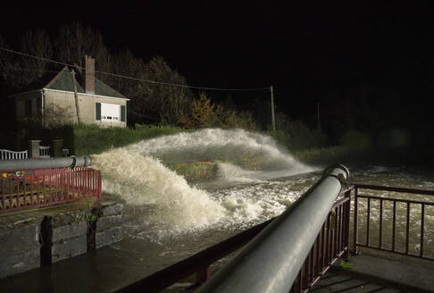 France, Hauts-de-France, Calais, Pumps pouring water from flooded area into canal at night - MKJF00052