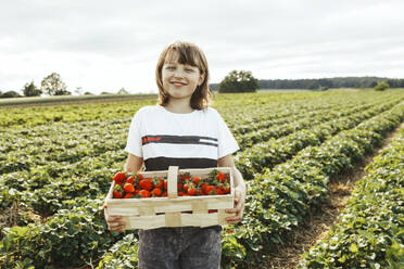 Smiling girl holding basket of strawberries in field - ELMF00008
