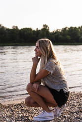 Smiling young woman crouching at beach on sunny day - UUF31422