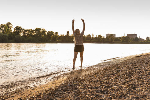 Junge Frau steht mit erhobenen Armen am Strand - UUF31424