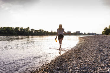 Frau geht mit Flasche im Meerwasser bei Sonnenuntergang - UUF31427