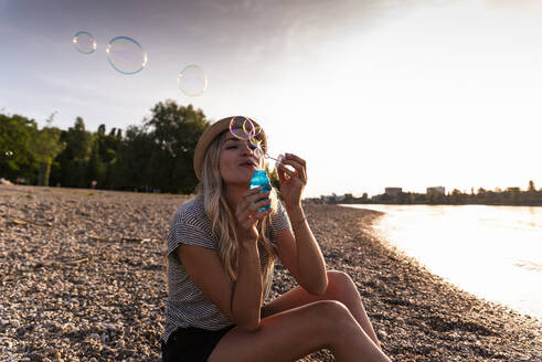 Woman blowing bubbles with wand at beach - UUF31428