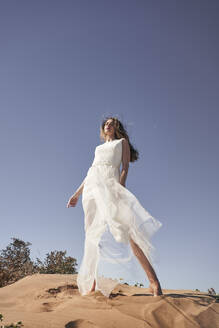 Braut trägt weißes Hochzeitskleid und steht auf Sand unter Himmel - VEGF06252