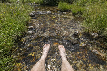 Switzerland, Valais Canton, Man dipping feet in clear stream - RUEF04326
