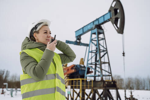 Ingenieur mit Schutzhelm und Gespräch über Walkie-Talkie auf einem Ölfeld - OLRF00193