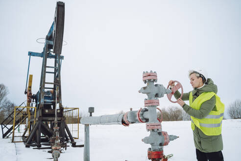 Engineer operating wellhead near drilling tower at oil field in winter - OLRF00199