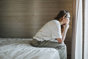 Stressed woman leaning on elbows and looking out of window at home - OLRF00201