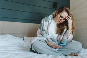 Enttäuschte Frau, die ihr Smartphone im heimischen Schlafzimmer benutzt - OLRF00203