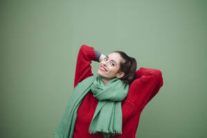 Smiling woman with hands behind head against green background - AMWF02044