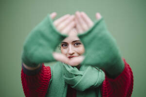 Frau blickt durch Fingerrahmen vor grünem Hintergrund - AMWF02048