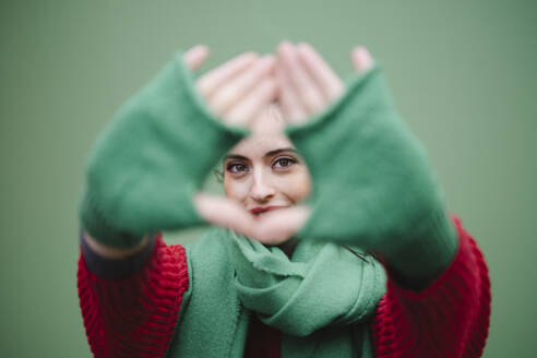 Woman looking through finger frame against green background - AMWF02048