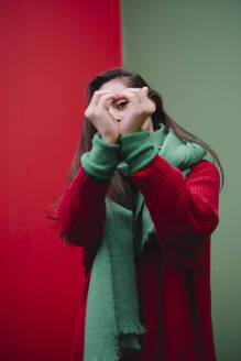 Woman gesturing heart shape in front of wall - AMWF02058