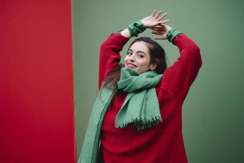 Happy woman with arms raised standing in front of wall - AMWF02062