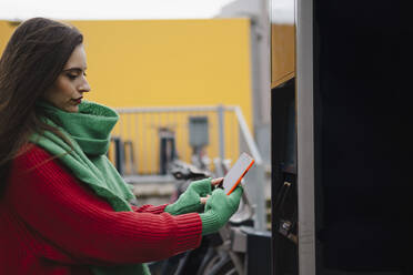 Frau beim Bezahlen mit dem Smartphone an einer Bikesharing-Station - AMWF02070