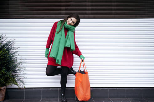 Lächelnde Frau steht mit orangefarbener Tasche vor einem Fensterladen - AMWF02071