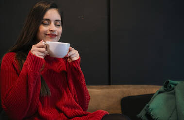 Lächelnde Frau mit geschlossenen Augen hält Kaffeetasse im Café - AMWF02080
