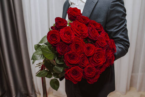 Teenage boy holding bouquet of red roses at home - MDOF01834