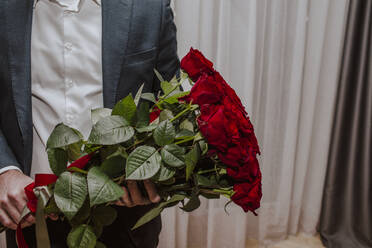 Junge im Anzug und mit einem Strauß roter Rosen in der Hand zu Hause - MDOF01835