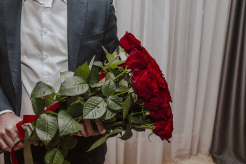 Boy wearing suit and holding bouquet of red roses at home - MDOF01835
