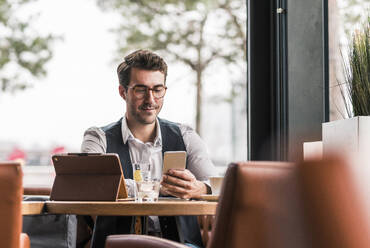 Businessman using smart phone at coffee shop - UUF31438