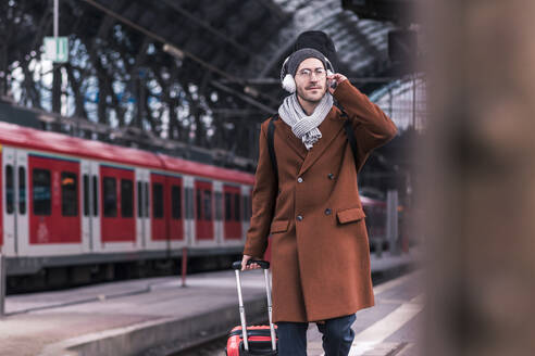 Geschäftsmann mit drahtlosen Kopfhörern, der auf einem Bahnsteig geht - UUF31442