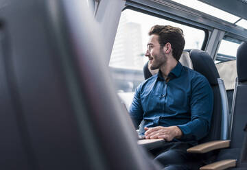 Smiling businessman looking out of window in train - UUF31447