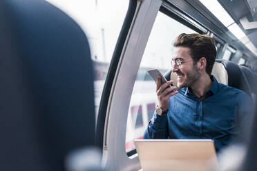 Happy businessman talking on smart phone in train - UUF31448