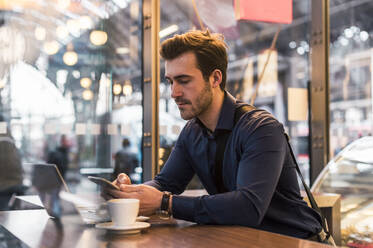 Businessman using smart phone near laptop at coffee shop - UUF31452