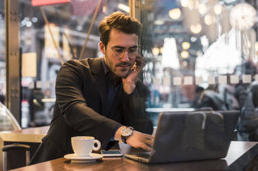 Businessman working on laptop in coffee shop - UUF31453