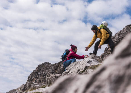 Mann hilft seiner Freundin beim Klettern auf einen Berg in den bayerischen Alpen, Deutschland - UUF31460