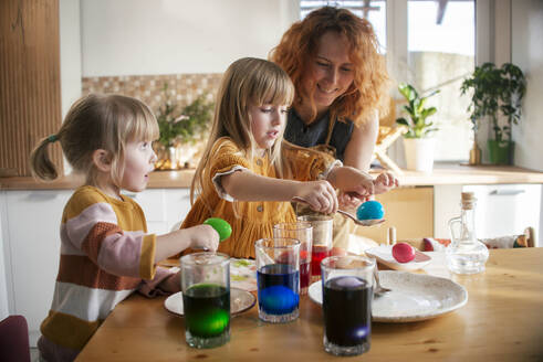 Mother and daughters dyeing Easter eggs at home - ASHF00054