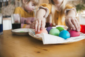 Mädchen arrangiert bunte Ostereier in einem Teller auf dem Tisch zu Hause - ASHF00056