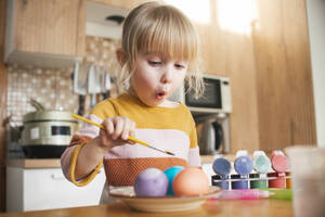 Surprised girl coloring Easter eggs with paintbrush at home - ASHF00059