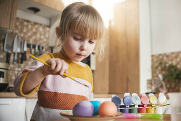 Nettes Mädchen färbt Ostereier mit Pinsel zu Hause - ASHF00060