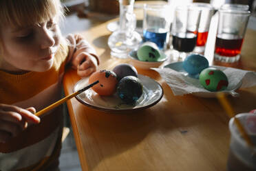 Mädchen dekoriert Ostereier mit Pinsel zu Hause - ASHF00062