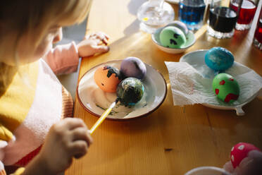 Mädchen bemalt Ostereier auf einem Teller zu Hause - ASHF00063