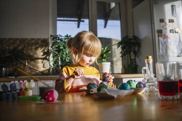 Niedliches Mädchen, das zu Hause Eier für Ostern dekoriert - ASHF00066