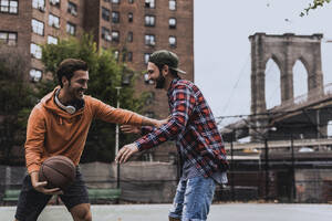 Junger Mann spielt Basketball mit einem Freund auf einem Platz in der Stadt - UUF31480