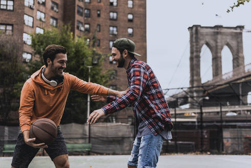 Junger Mann spielt Basketball mit einem Freund auf einem Platz in der Stadt - UUF31480