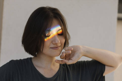 Frau mit regenbogenfarbener Lichtreflexion im Gesicht - MCHF00003