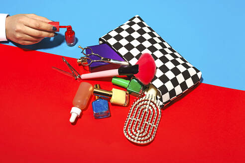 Studio shot of female hand touching cosmetics falling out of checked purse - RDTF00041
