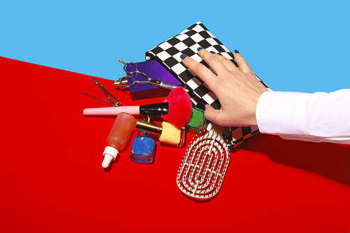 Studio shot of female hand touching cosmetics falling out of checked purse - RDTF00042